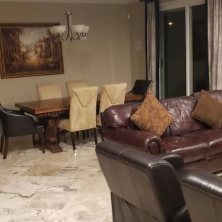 A cozy living and dining area featuring a leather sofa, a dining table with chairs, a painting on the wall, and a chandelier.