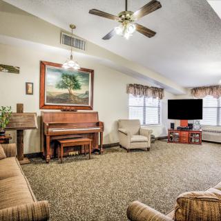 A cozy living room featuring a piano, ample seating, and a large television.