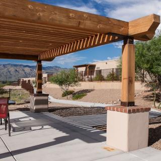 A wooden pergola providing shade in a desert backyard setting with patio furniture.
