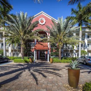 A vibrant entrance to a residential building surrounded by lush palm trees and clear blue skies.