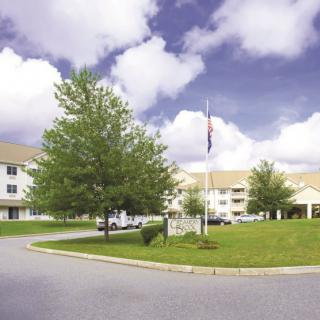 A peaceful residential building surrounded by trees and a grassy area with a flagpole, under a cloudy sky.