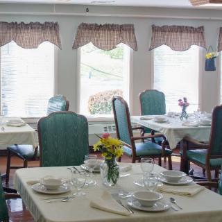 A cozy dining room with tables and chairs, elegantly set with tableware and decorated with small flower arrangements.