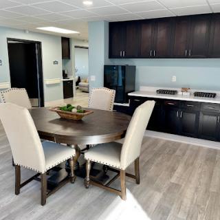 A modern kitchen and dining area featuring a round table with chairs, sleek black cabinets, and a light-colored floor.