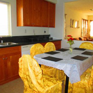 A cozy kitchen and dining area with a table set for four, adorned with a flower vase and yellow chair covers.