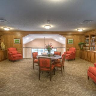 A cozy reading room with plush armchairs, a central table, and bookshelves lining the walls.