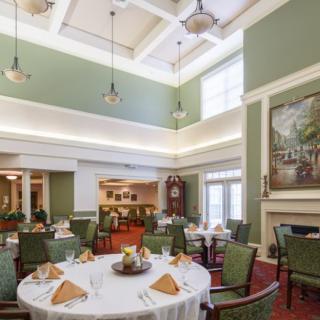 A spacious and elegantly decorated dining room with neatly arranged tables and chairs, featuring a high ceiling and soft lighting.