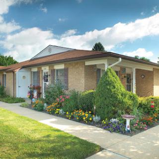 A charming single-story house surrounded by a well-maintained garden, set against a picturesque sky.