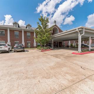 A brick building with a parking lot and several cars parked under a partly cloudy sky.