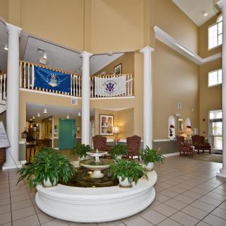 A spacious lobby featuring a central fountain, indoor plants, and decorative flags.