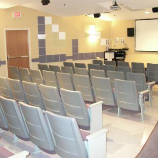 An empty auditorium with rows of chairs facing a projector screen.