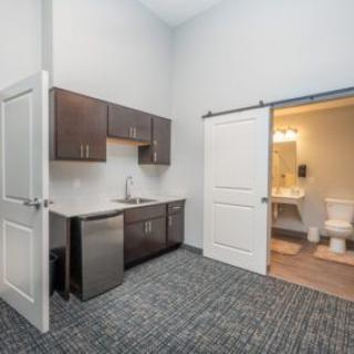 A modern office space featuring a kitchenette with cabinets and an adjacent bathroom.