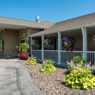 A charming building with a covered porch, surrounded by a well-maintained garden featuring vibrant flowers and greenery under a clear blue sky.