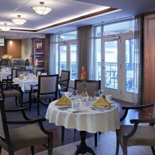 An elegant dining room with well-set tables and chairs, featuring large windows for natural lighting.