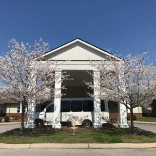 A van parked under the entrance of a building surrounded by blossoming trees on a sunny day.