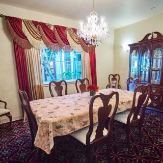 A formal dining room with elegant furnishings, featuring a chandelier and richly draped curtains.