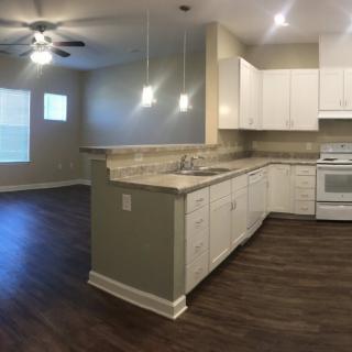 A modern kitchen with an open floor plan, featuring white cabinets and wood flooring.