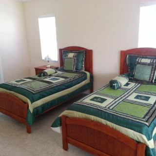 A bedroom featuring two twin beds with green and black bedding, accented by a small lamp on a bedside table.