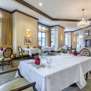 An elegant restaurant dining room with beautifully set tables, ornate chairs, and a chandelier.