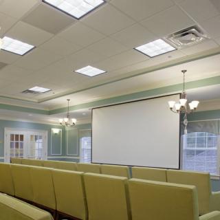A well-lit conference room with rows of seating and a large projector screen.