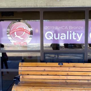 A bench in front of a window displaying a sign with the word 'Quality'.