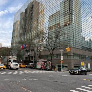 A bustling street scene in New York City featuring a modern glass building and various vehicles.