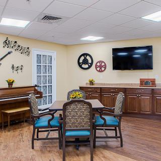 A cozy dining and recreation room featuring a piano, dining table with chairs, wall decorations, and a mounted TV.