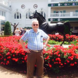 A man stands in front of a horse statue surrounded by flowers.