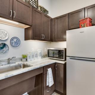 A modern kitchen with dark wooden cabinets, a stainless steel refrigerator, and a microwave on the countertop.