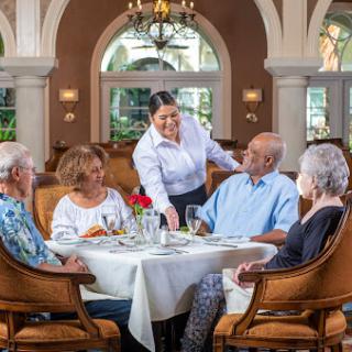 A group of elderly guests enjoying a meal at a beautifully set table, with attentive service from the waitstaff.