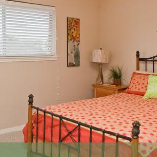 A cozy bedroom featuring a metal bed frame with colorful bedding, a nightstand with a lamp, and decorative wall art.