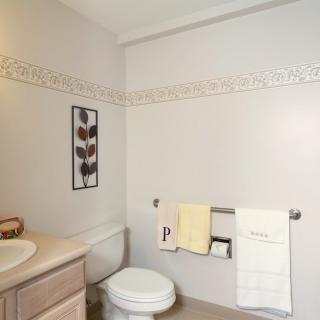 A neatly arranged bathroom featuring a toilet, sink, and towels with decorative wall art and a tile border.