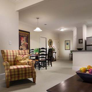 A cozy living and dining area featuring a plaid armchair, artwork on the wall, and an open kitchen.