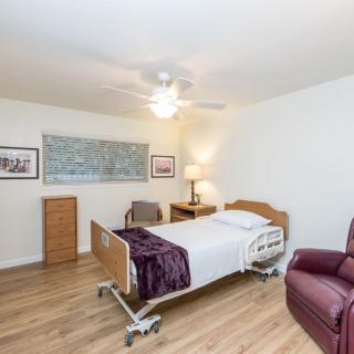 A well-lit room with a hospital bed, recliner, and wooden flooring.