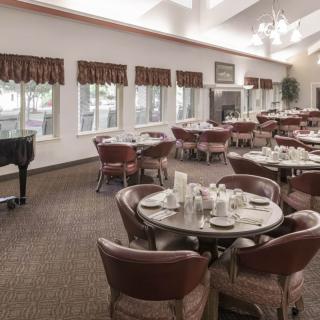 A spacious dining room with neatly arranged tables and chairs, featuring a piano in the corner.