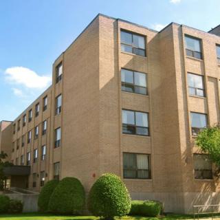 A brick apartment building with multiple windows and neatly trimmed shrubs in the foreground.
