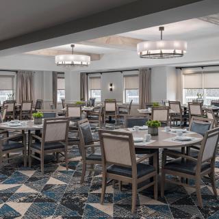 A spacious dining room with neatly arranged tables and chairs, featuring modern lighting fixtures and a patterned carpet.