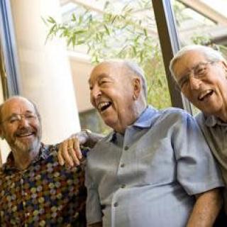 Three elderly men laughing and enjoying each other's company indoors.