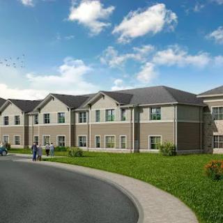 A modern residential apartment complex with a well-maintained lawn and clear blue sky.