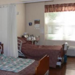 A hospital room with two beds separated by a curtain and a window letting in natural light.