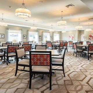 An elegant dining room featuring neatly arranged tables and chairs, with modern lighting and a patterned carpet.