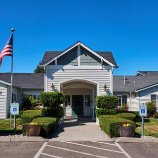 A well-maintained building entrance with an American flag and surrounding greenery on a clear, sunny day.
