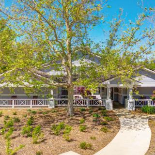 A charming house with a well-kept yard, featuring a large tree and a winding path leading to the entrance.
