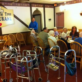 A group of seniors dining together in a restaurant with multiple walkers nearby.