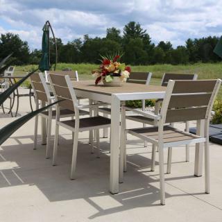 An outdoor patio dining set with a table and chairs, set against a backdrop of greenery.