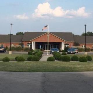 A single-story brick building with an American flag in front, flanked by a parking lot and greenery.