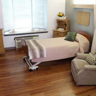 A comfortable hospital room with a bed, armchair, and wooden furniture.