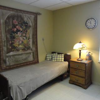 A cozy bedroom featuring a single bed, a decorative wall hanging, a bedside lamp, and a clock.
