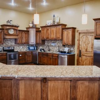A modern kitchen with wood cabinets and a granite countertop, featuring stainless steel appliances and pendant lighting.