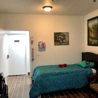 A cozy room featuring a bed with green bedding, artwork on the wall, and a wheelchair, providing a comfortable living space.