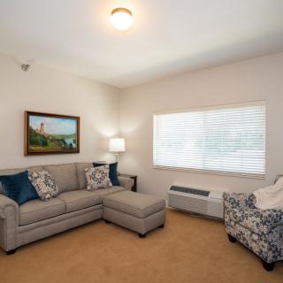 A cozy living room featuring a sofa, an ottoman, and a patterned armchair, with natural light streaming in through the window.